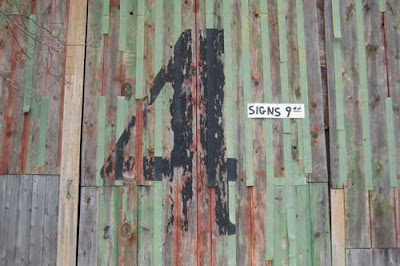 Green barn wall with multiple colors of paint showing through, and a large serif number 4 painted on it, weathered as well