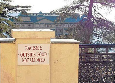 Sign along a railing overlooking a picturesque building reading Racism & Outside Food Not Allowed