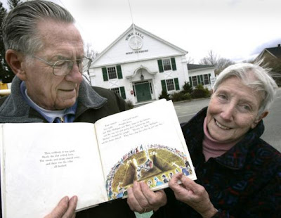 Photo of an elderly man (with his smiling wife) holding a book open to an illustration of the steam shovel in the bottom of a brown pit