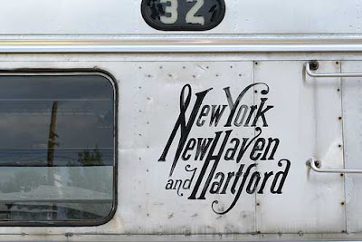 Lettering on the side of a silver train, reading New York New Haven and Hartford, with the Ns shared and the Hs shared