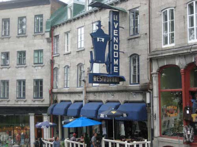 Weathered, blue metal sign saying La Vendome with an old-fashioned carriage below the name