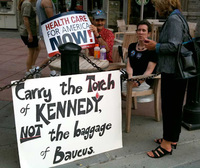 Couple with a sign reading Carry the torch of Kennedy, not the baggage of Baucus