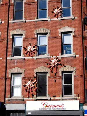 Five shiny metal sculptures that look like splatted amoebas attached to a brick commercial building