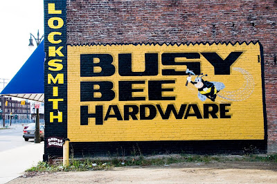 Yellow and black hand-painted Busy Bee Hardware sign on brick building