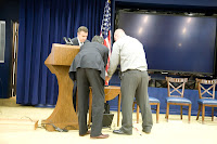 Men on stage fiddling with AV, black screen