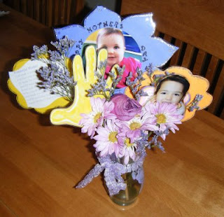 Flowers in a vase with paper cutouts inserted of hand prints and faces of children