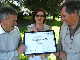 Una Anderson Ryan, Chairperson of the Parkinsons Association of Ireland (PAI), displays Muhammad Ali's Honorary President Award to Billy Rice & Sid Rellis of the Mid-West Parkinsons Association, beneath the shaking leaves of an Aspen Tree – on which the green PAI logo is based.