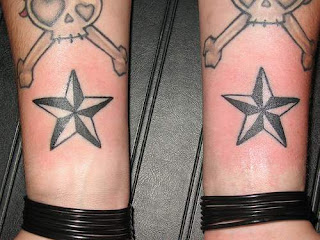 Estrelas gemeas tatuadas nos pulsos, ornamentadas por uma tatuagem de caveira