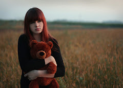 A girl with brown hair holding a brown teddy bear.