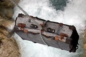 A suitcase hanging from a chain, precariously, over rushing water.