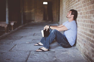 man with a bible sitting against a wall