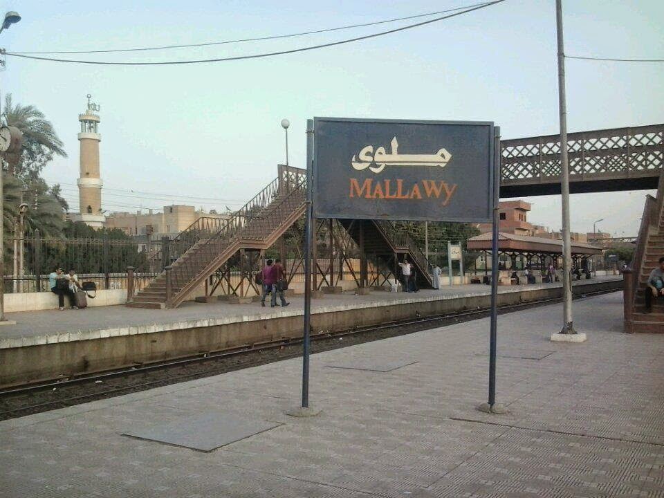 اللافتة الجديدة لمحطة قطار ملوى وخلفها الكوبرى المعدنى وخلفهما يظهر مسجد الرى