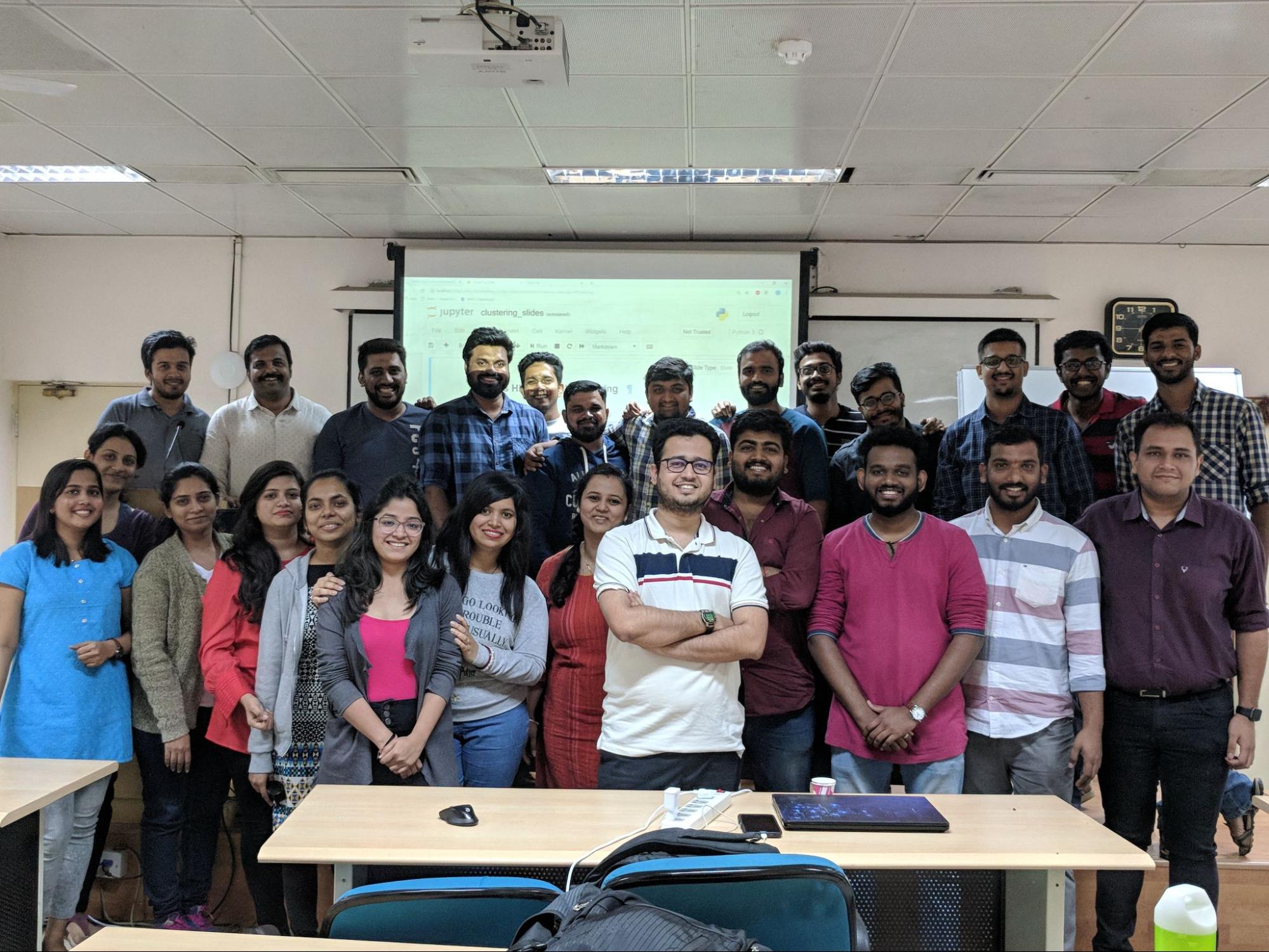 Image shows Bhavesh Bhatt standing in the center of a group of people standing in a classroom and smiling for the camera