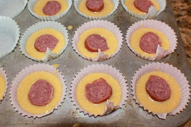 this is a muffin tin filled with cornbread batter and kielbasa in the center