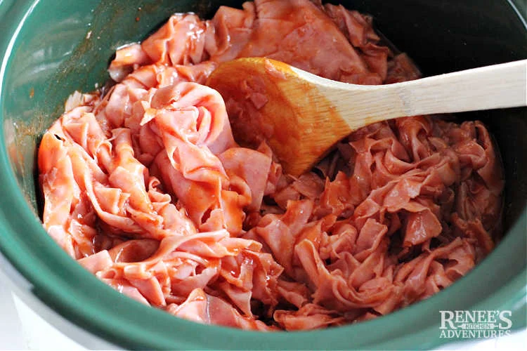 Stirring ham and BBQ sauce in slow cooker with a wooden spoon