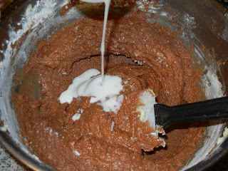 pouring cream into the batter with a black plastic spoon to the right 