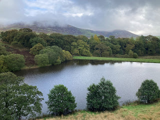 A photograph of a view over Morton Loch showing trees in the foreground and hills in the background.  This being a view from the eastern tower of Morton Castle.  Photograph by Edie Lettice for the Skulferatu Project.