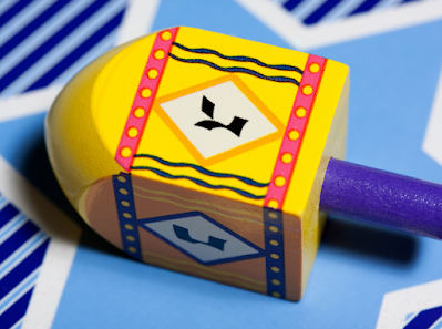 Photo of a yellow dreidel with the letter gimmel facing upwards.