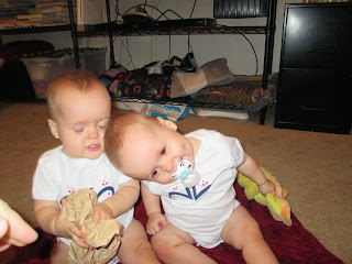 twin baby girls, one leaning her head on the other's shoulder and smiling around her pacifier