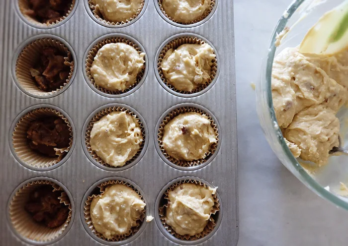 scooping muffin batter over topping into baking cups