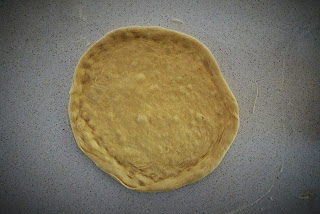 A circular, flattened pizza base, viewed from directly above