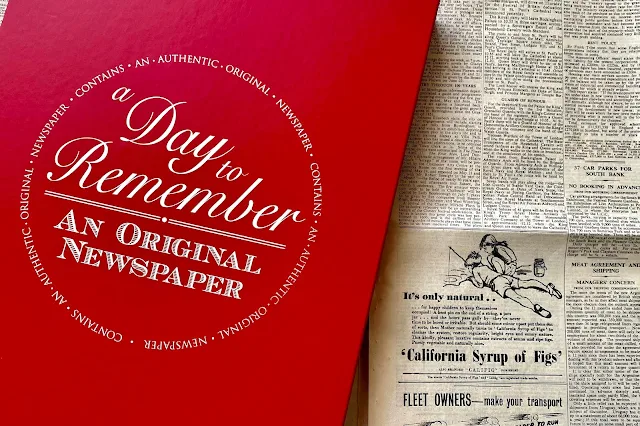 A red classic gift box with "a day to remember and original newspaper" next to an authentic newspaper
