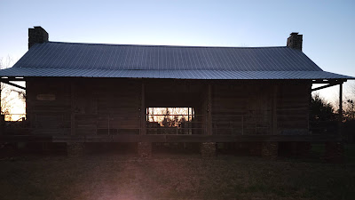 The sun setting through the dogtrot of the Barnard-Newell Log House, situated just above the troop's campsite.