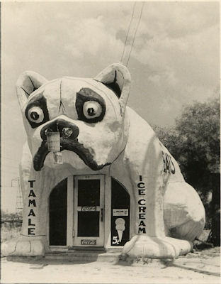 A black-and-white photograph of a restaurant shaped like a bulldog. "TAMALE" is written on the bulldog's left leg. "ICE CREAM" is written on the bulldog's right leg.