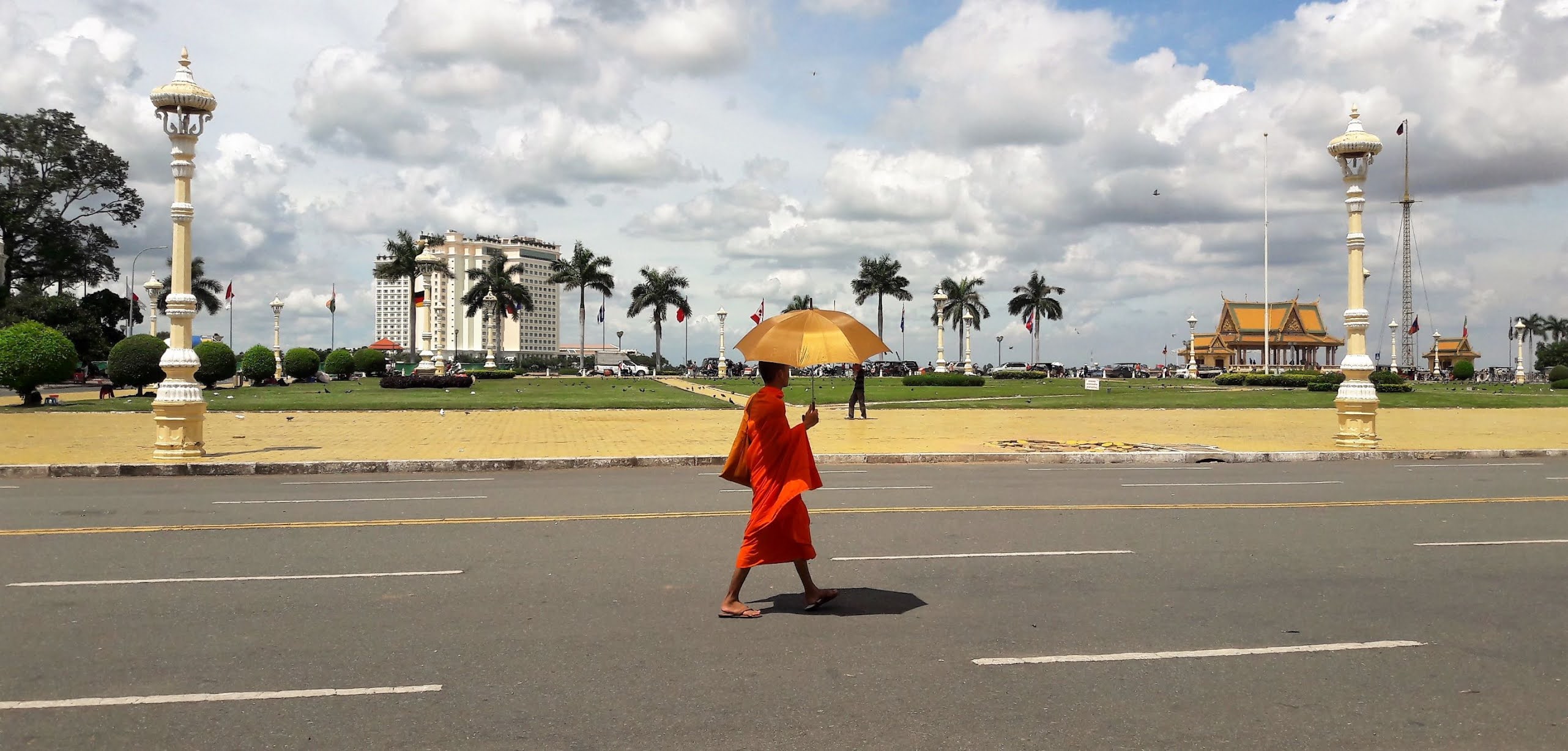Buddhist monk holding a yellow umbrella walking alone in the street.