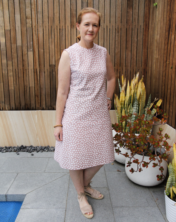 a photograph of a white woman posing in a pink polka dress beside some plants in white pots