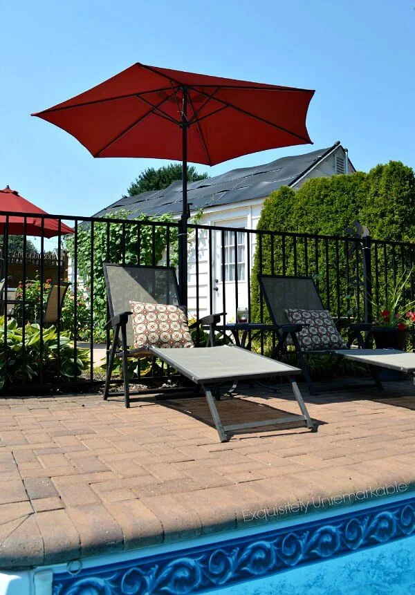 Brick pool patio with red umbrella and lounge chairs with Pillows