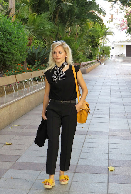 Alejandra Colomera con camiseta negra, pantalón formal negro, lazo en el cuello negro con lunares blancos y complementos mostaza