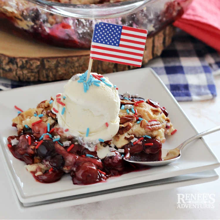 Red, White, and Blueberry Dump Cake Recipe slice on white plate with scoop of vanilla ice cream and patriotic sprinkles.