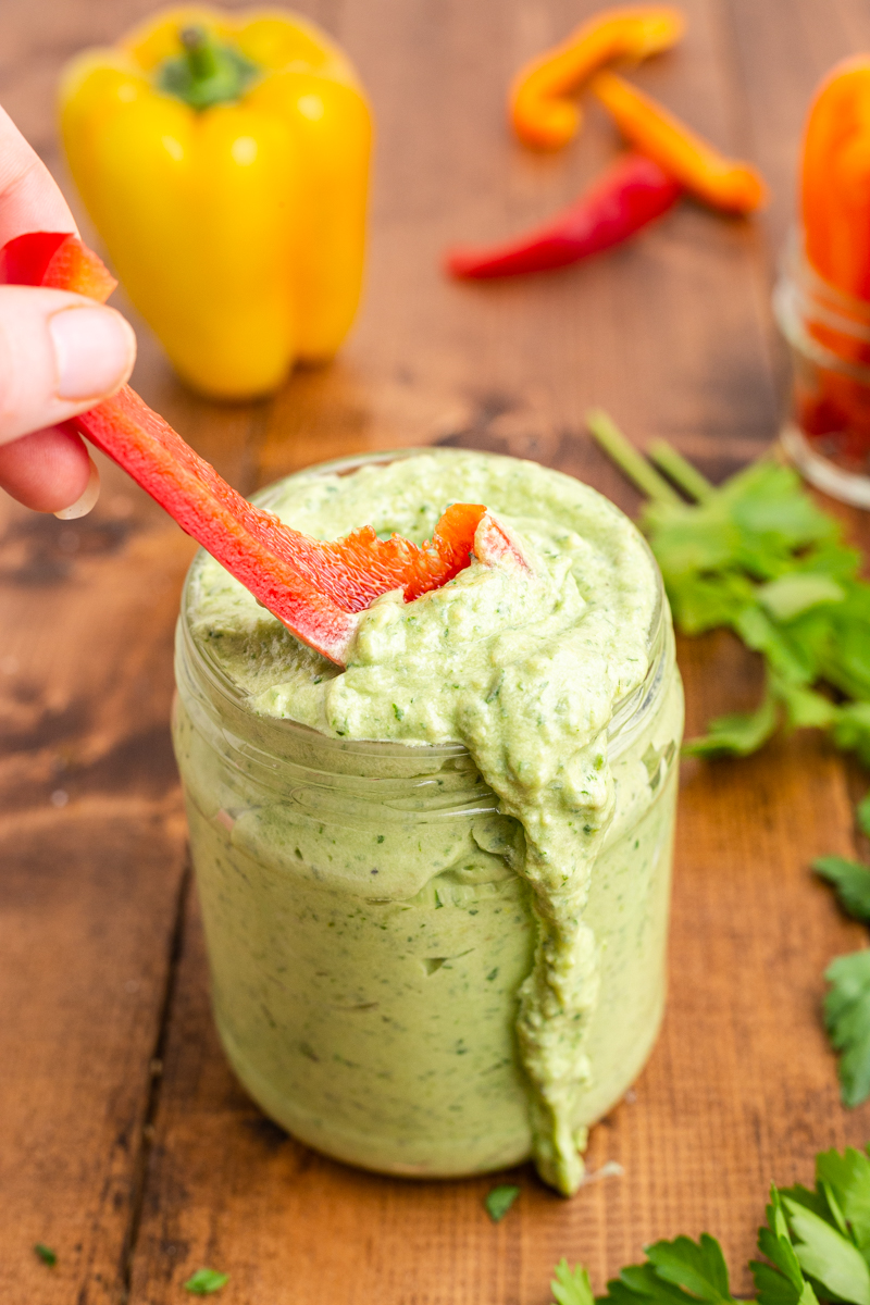 Closeup phot of Avocado Ranch Dressing and Dip in a mason jar with someone dipping a slice of bell pepper into it,