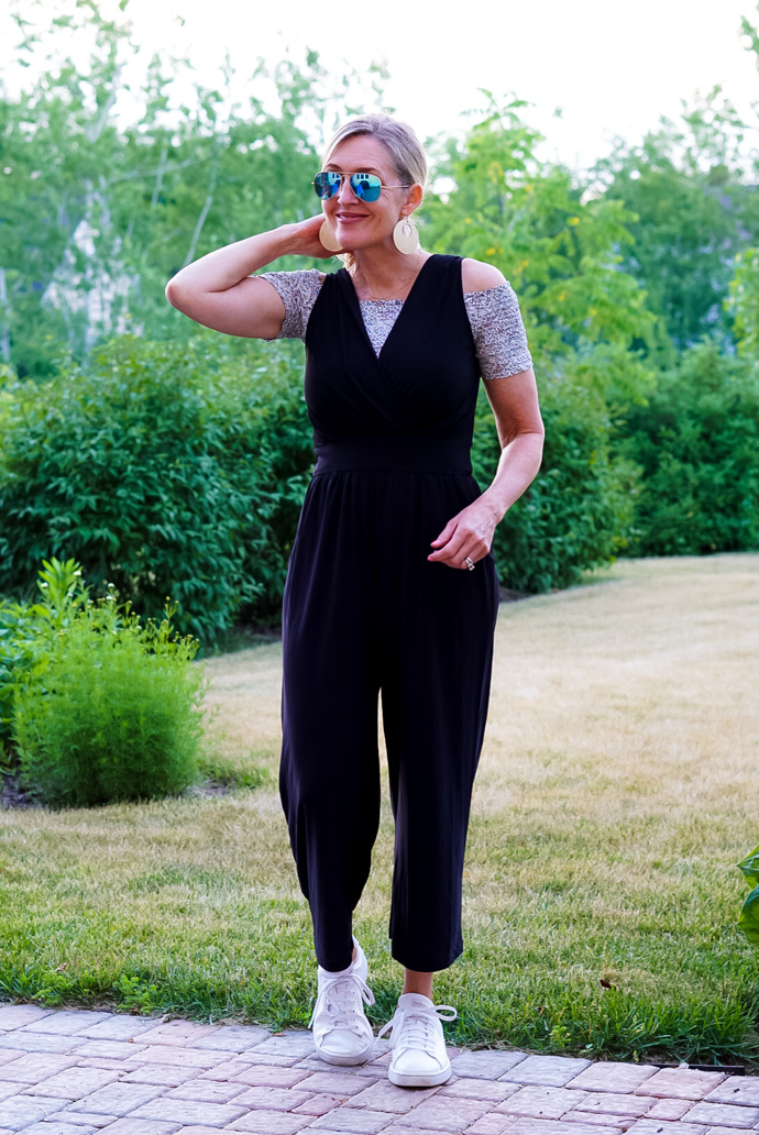 A woman stands in front of a green lawn wearing a black jumpsuit