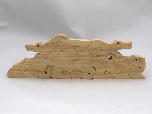 A photo of a handmade wood alligator family stacking puzzle with the mother alligator and five baby alligators.