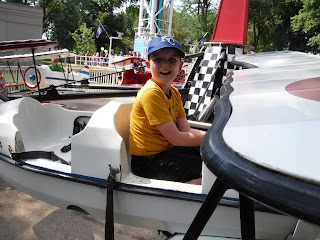 a boy in a yellow shirt and blue baseball cap sits in a white airplane ride at Adventureland Park in Altoona, Iowa