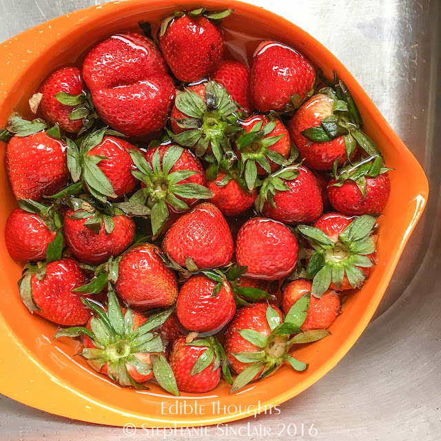 Image from above at an orange mixing bowl filled with water and whole strawberries.