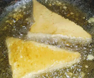 Deep frying triangular shape bread pakora in hot oil