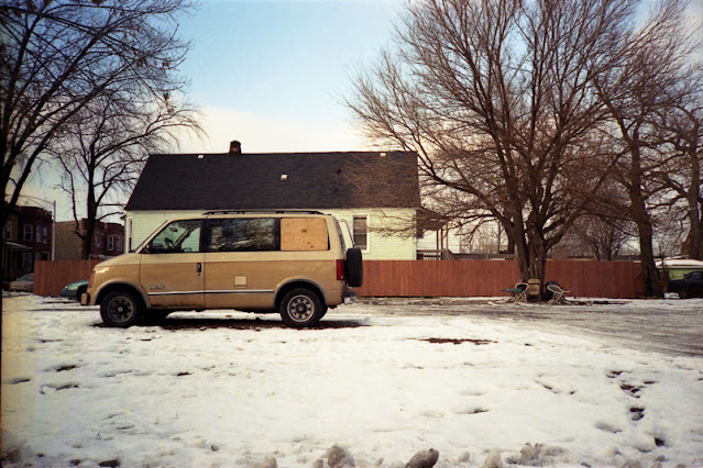 Two-toned tan van parked in an empty lot in front of a house in Chicago