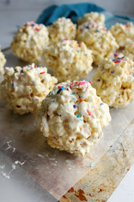 These soft and sweet popcorn balls are simple to make with marshmallows and popcorn. They sprinkles add an extra fun touch! close up of marshmallow popcorn balls with sprinkles on top sitting on wax paper lined baking tray