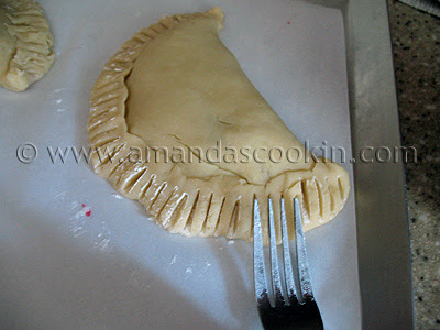 A photo of a fork crimping the edges of an unbaked cherry hand pie.