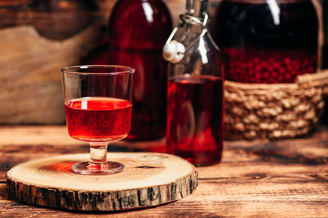 kieliszek czerwonego wina na drewnianej podstawce - w tle butelka