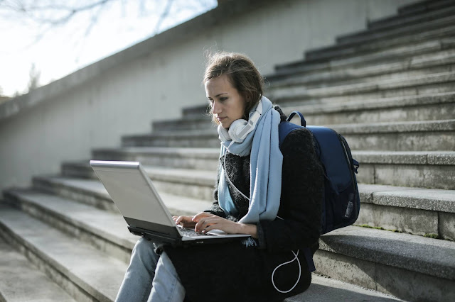 A university student sat on steps with their grey laptop