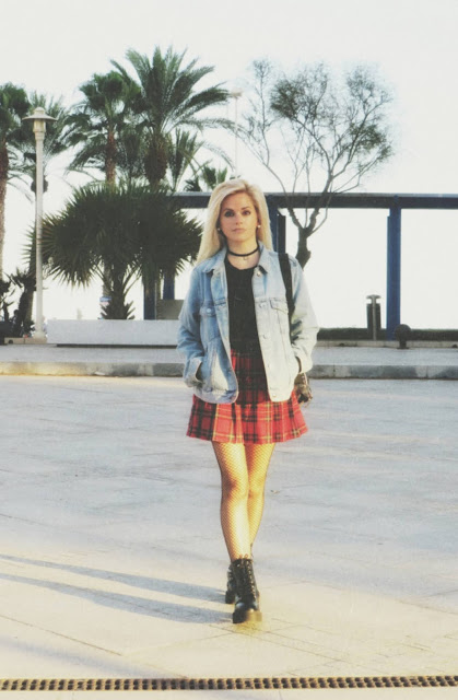 Estilo grunge con camiseta negra, falda de tablas tartán, medias de red grande, botas estilo militar y cazadora vaquera