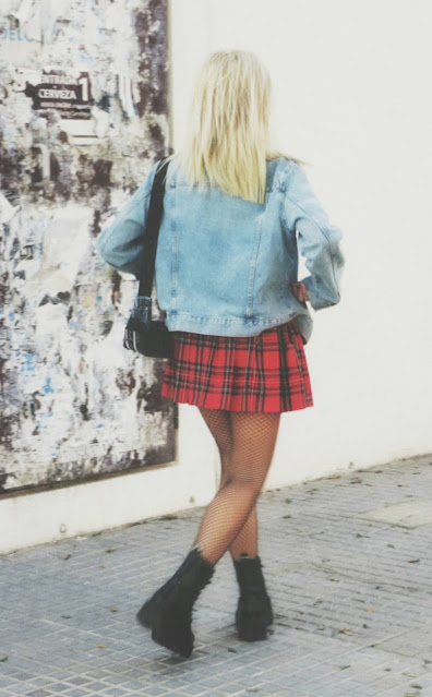 Estilo grunge con camiseta negra, falda de tablas tartán, medias de red grande, botas estilo militar y cazadora vaquera