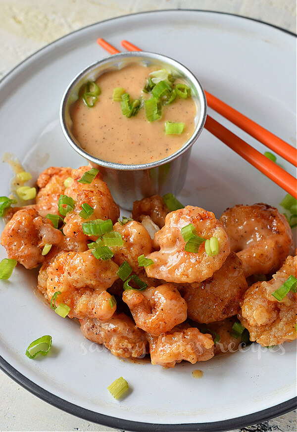 Try this quick,easy and best copycat bonefish grill bang bang shrimp recipe with amazing bang bang sauce. The shrimp are crispy fried or for a healthy option air fry them or bake further toss them in sweet and savory sauce.You can serve this with rice,or with pasta,in rice bowl or in Asian salad. #savorybitesrecipes #bangbangshrimp #bonefishgrill #appetizer #recipe #shrimp #copycatrecipe top view of white plate with crispy bonefish grill style bang bang shrimp