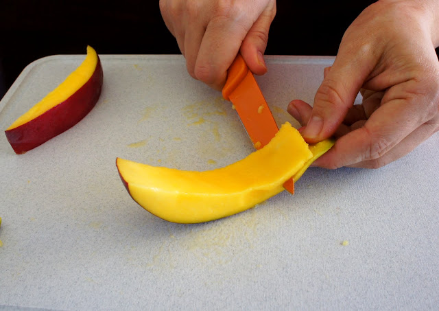 A hand using a knife to demonstrate how to cut a mango