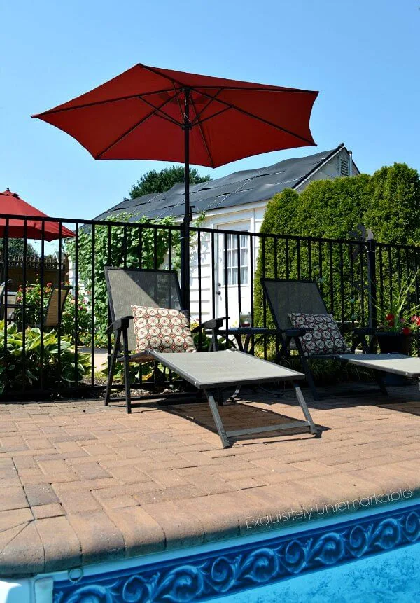 Two chaise lounges with red umbrella by pool