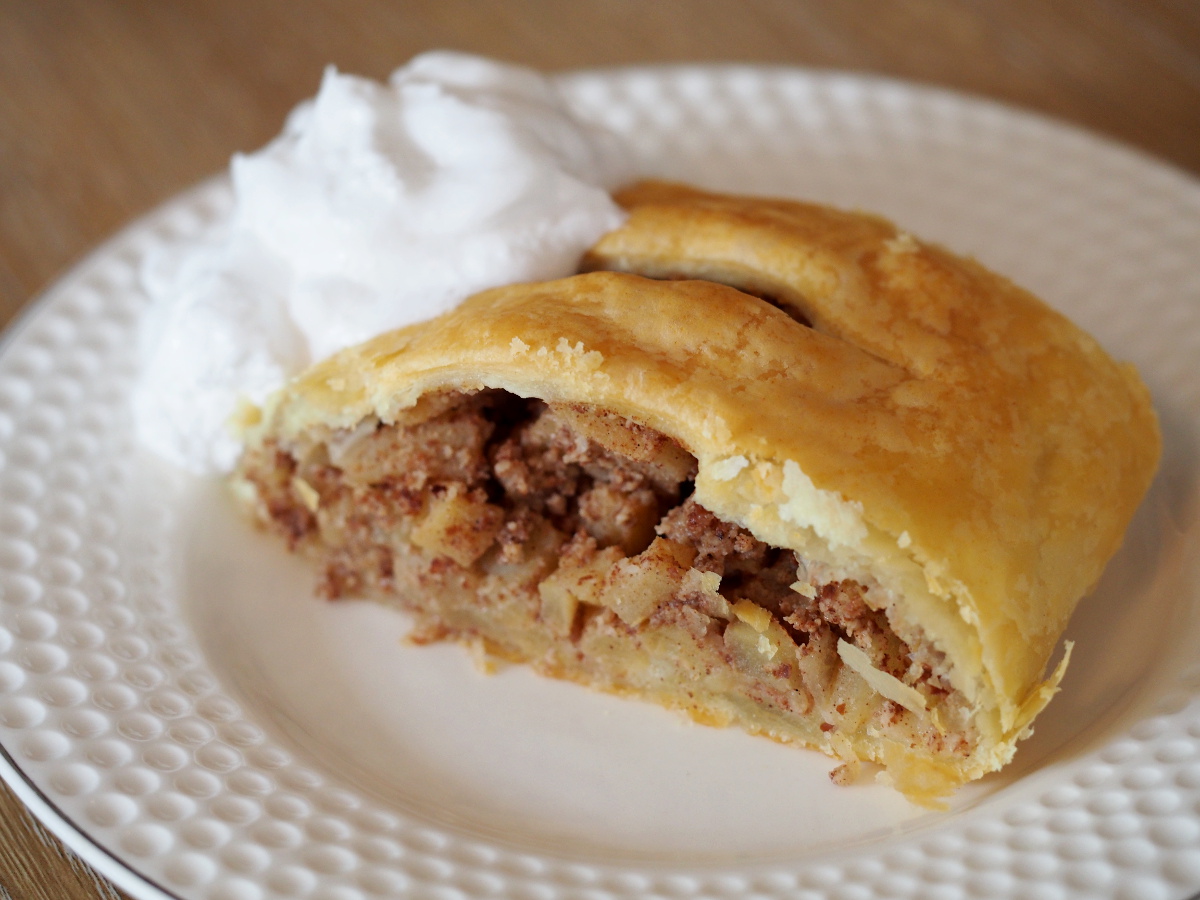 Ein Stück Apfelstrudel auf einem Teller mit etwas Schlagcreme daneben.